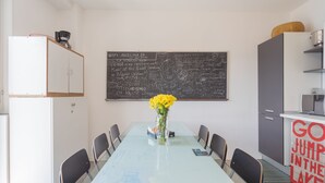 Een moderne eetruimte met een glazen tafel, stoelen, een vaas met gele bloemen en een schoolbord met teksten.