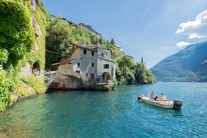 A stone building with a stone bridge, a boat with people, and a lake with mountains in the background. - La Civera - Nesso Lake Como - Co-f877-pont41ar (Nesso)