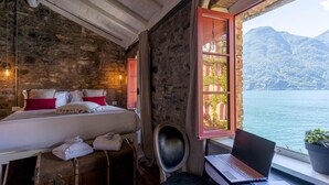 A rustic room with a bed, a suitcase, a laptop, and a view of a lake and mountains.