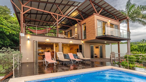 Ein modernes, zweistöckiges Haus mit Swimmingpool, Gartenmöbeln und einer überdachten Terrasse.