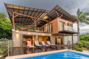 A modern two-story house with a swimming pool, outdoor seating, and a covered patio.
