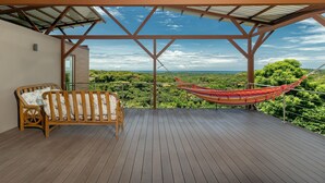 Eine Holzterrasse mit einer Hängematte und einer Holzbank, mit Blick auf eine üppige Landschaft.
