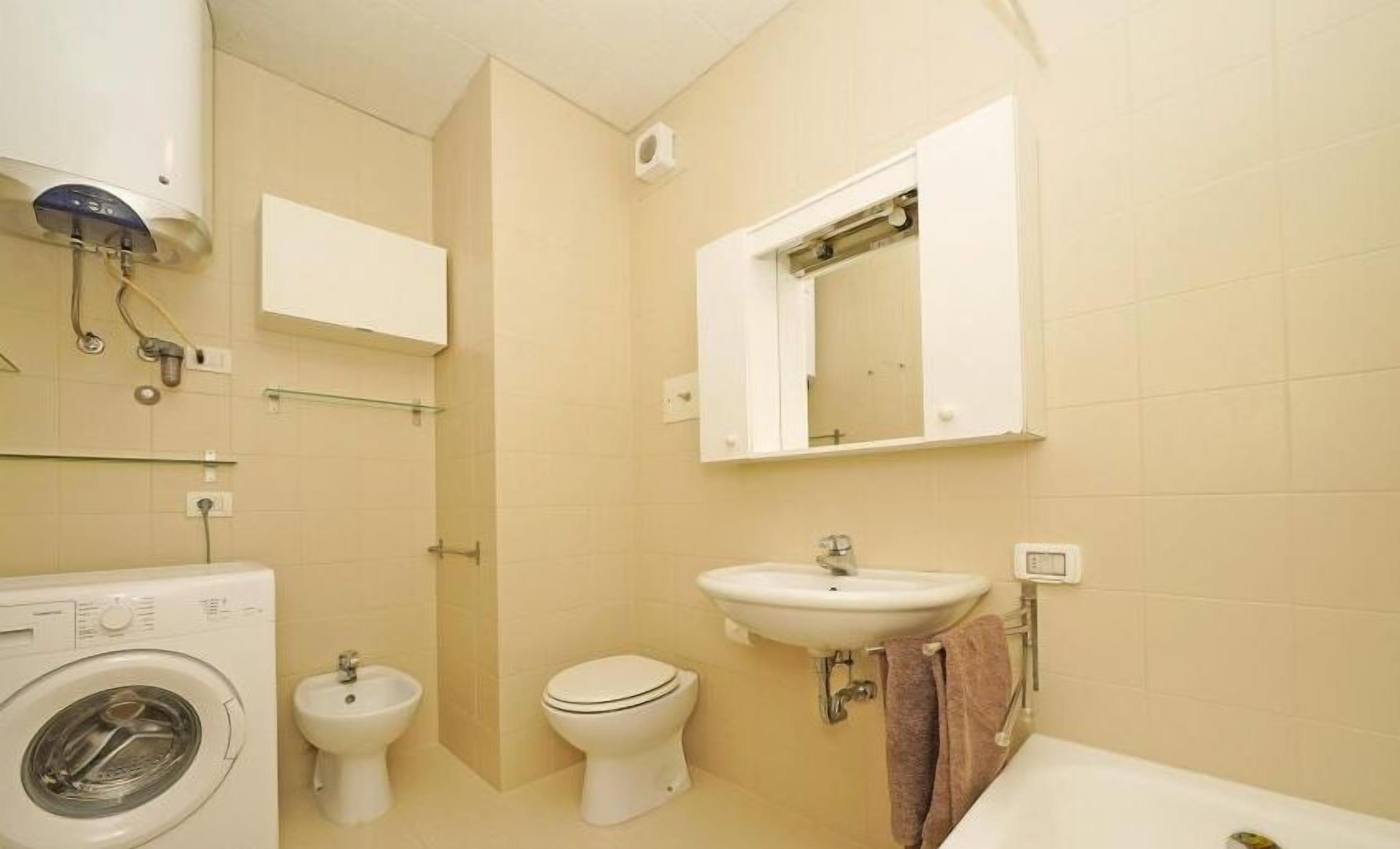 Une salle de bain compacte comprenant un lave-linge, un bidet, des toilettes, un lavabo et un miroir.