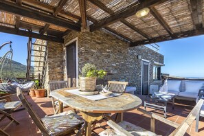 A stone building with a wooden table and chairs, a hanging chair, and a view of the sea. - Casa Li Nassi in Stintino (Stintino)