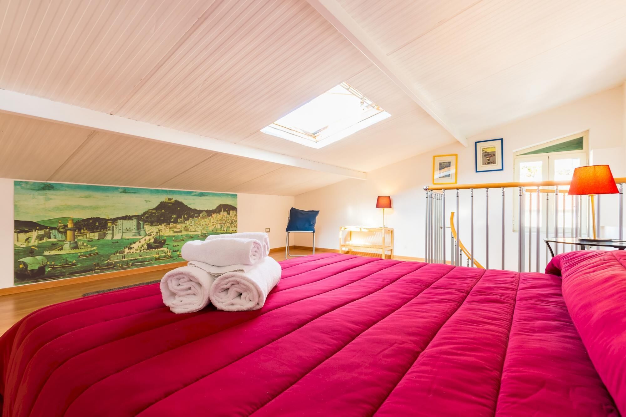 Ein Schlafzimmer mit einem großen Bett, einem Oberlicht, einem Landschaftsbild und einer Treppe.
