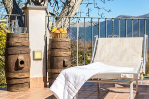 Un espacio al aire libre iluminado por el sol con una barandilla metálica, un pilar de piedra y una silla lounge con una toalla.