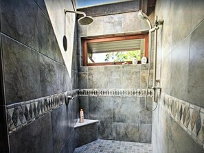 A small, tiled shower area with a window, a shelf with toiletries, and a showerhead.