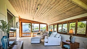 Una sala de estar acogedora, con techo de madera, ventanas amplias y vistas al verdor exterior.