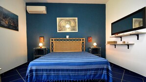 Een slaapkamer met een bed, twee nachtkastjes, een wandairconditioner, een lijst met een afbeelding en een spiegel.