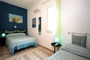 A bedroom with two beds, a window with a green curtain, a wall-mounted air conditioner, and a painting.