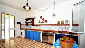 Een keuken met een wasmachine, een fornuis en een spoelbak. Er staat een mand met bloemen op de tafel.