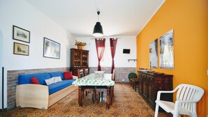 Een kamer met een bank, een eettafel en stoelen. Er is een kast en een hanglamp.