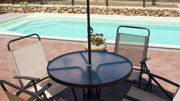 Eine Terrasse mit einem runden Tisch und Stühlen, einem Sonnenschirm und einem Pool mit Blick auf den Ozean.