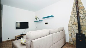 A living room with a beige sofa, a flat-screen TV, a stone wall, and a black guitar case. - Al080 Villa Stella Cinese con Piscina Privata (Alcamo)