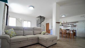 A living room with a beige sectional sofa, a dining area with a table and chairs, a kitchen with a refrigerator, and a spiral staircase. - Al080 Villa Stella Cinese con Piscina Privata (Alcamo)