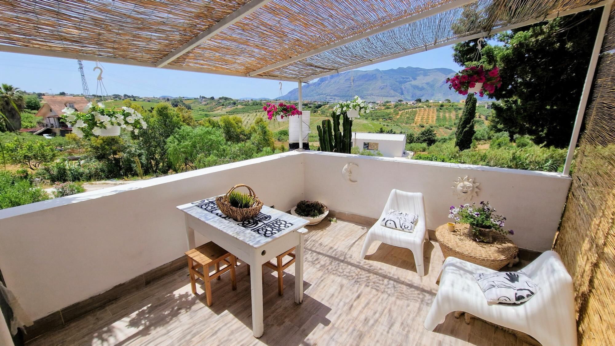 Un balcon avec une table, deux chaises, une jardinière suspendue et un élément décoratif mural.