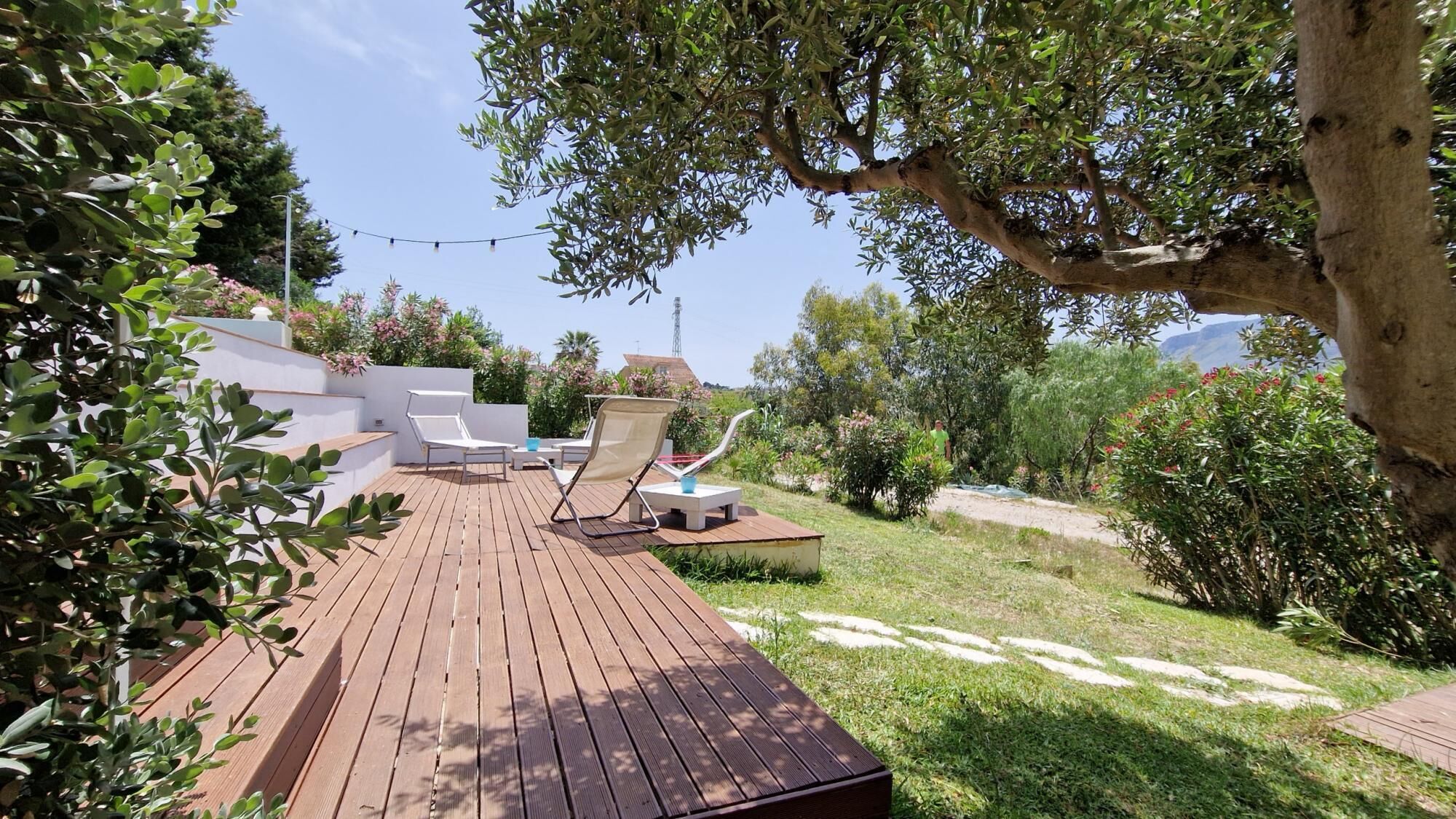 A wooden deck with lounge chairs and a small table, surrounded by greenery and a clear sky.
