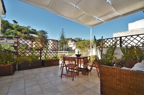 Relax in this serene outdoor space with a comfortable table and chairs, a wicker sofa, and lush greenery.