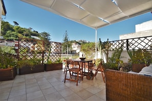 Relax in this serene outdoor space with a comfortable table and chairs, a wicker sofa, and lush greenery.