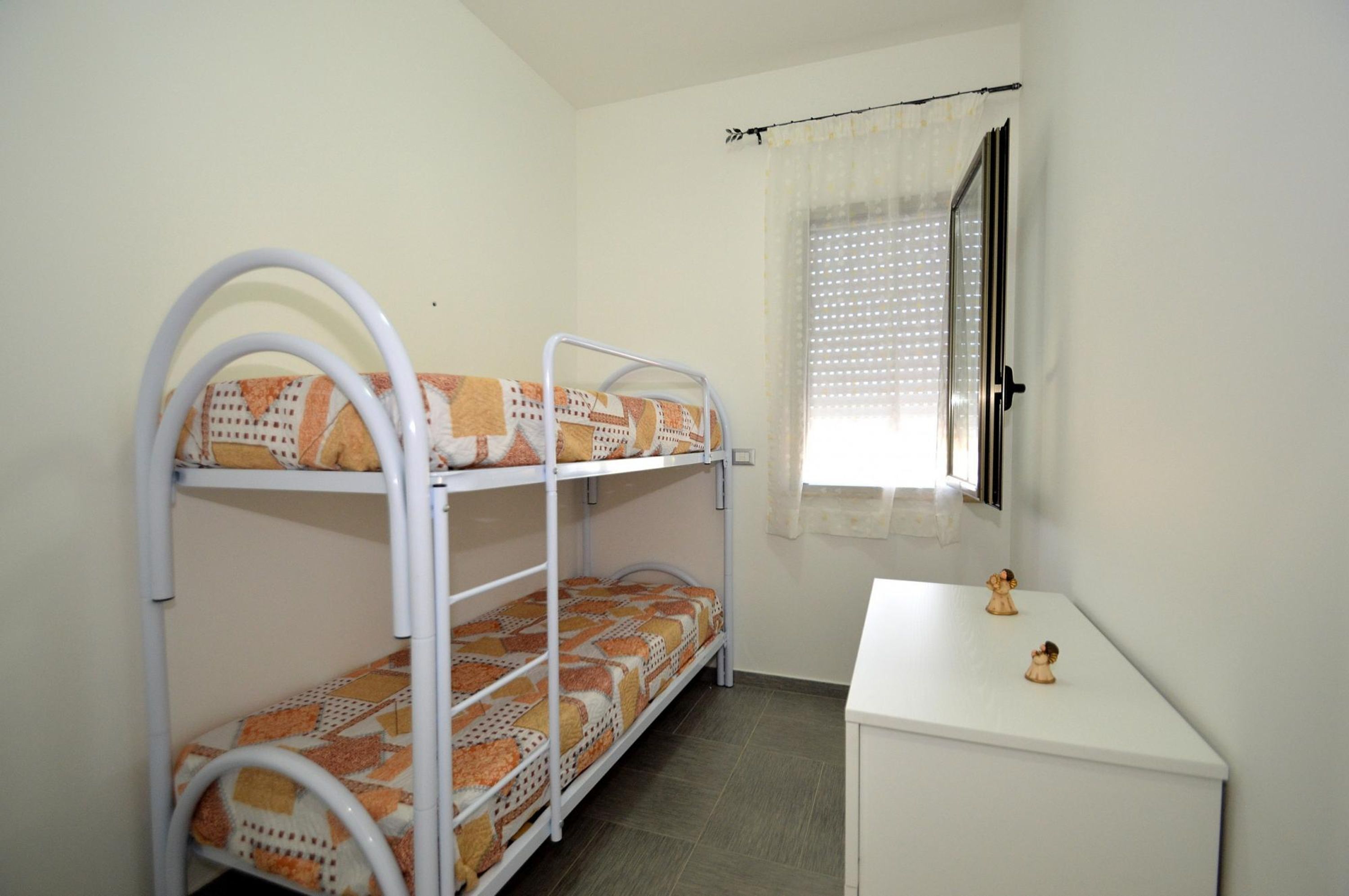 Habitación con literas, un pequeño escritorio blanco y dos figuras decorativas.