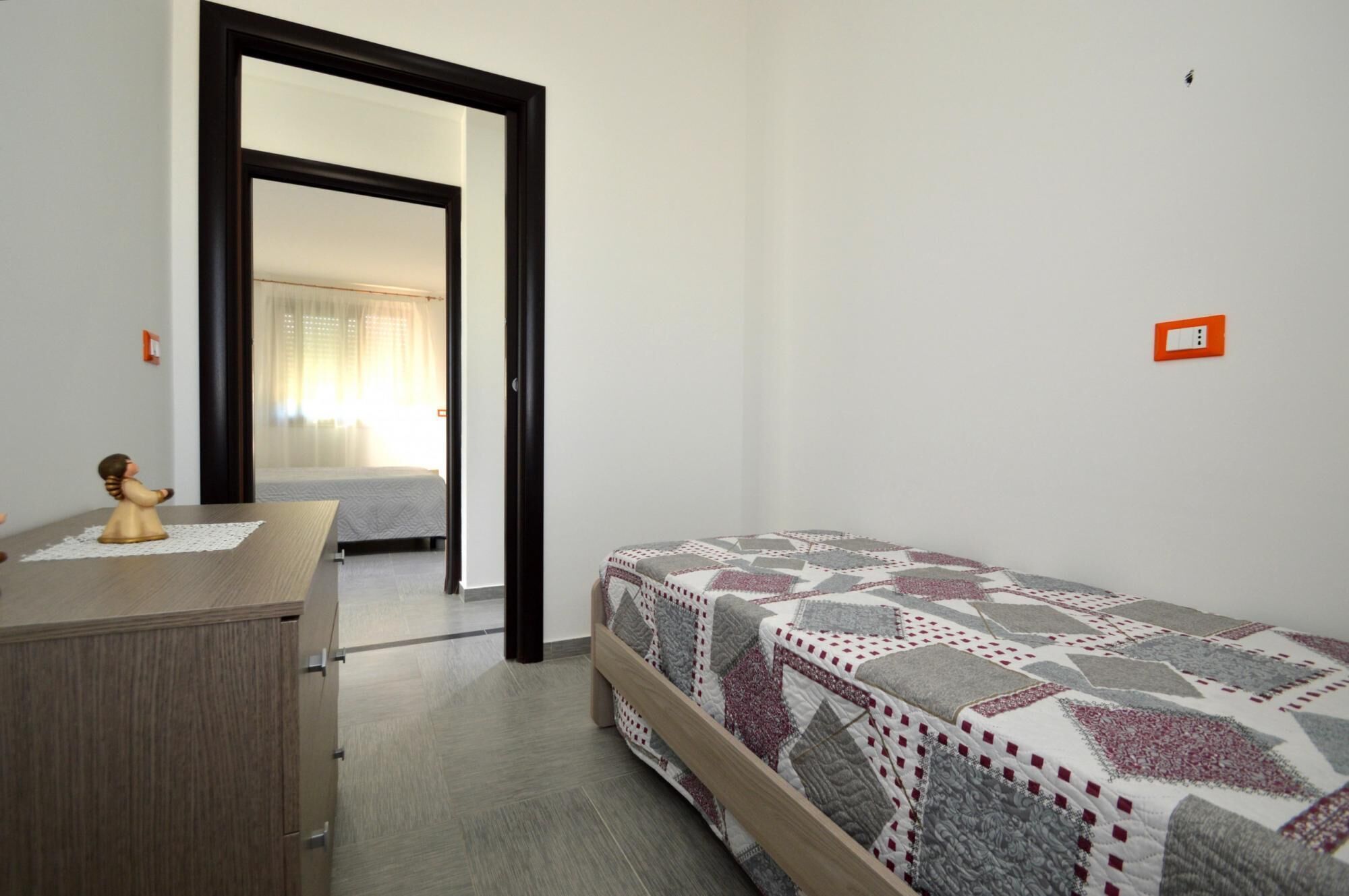 A bedroom with a bed, a dresser, and a door leading to another room.