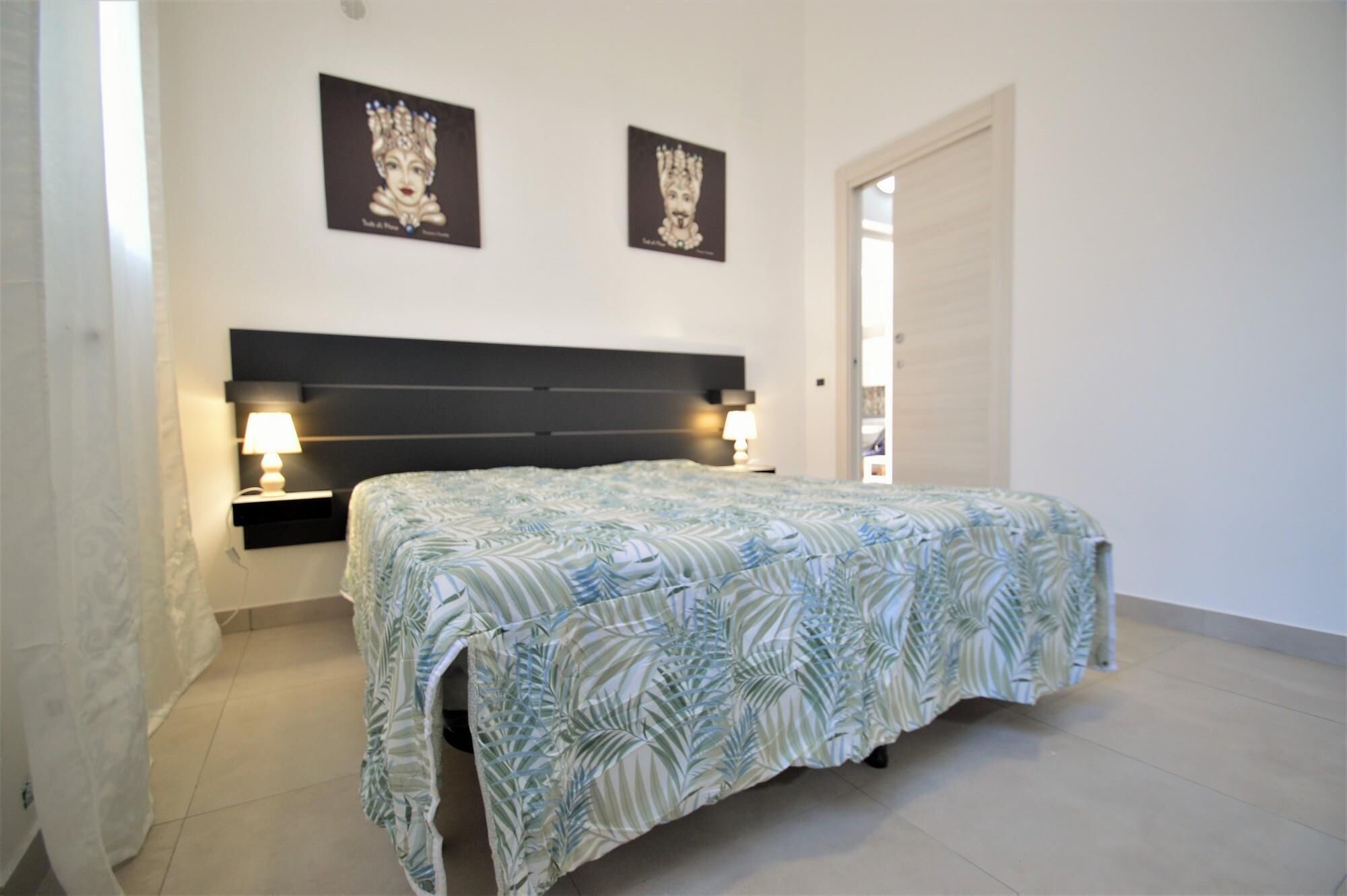 A bedroom with a bed, two wall-mounted lamps, and two framed pictures.