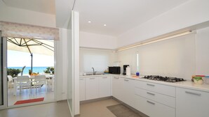 A modern kitchen with white cabinets, a gas stove, and a view of the ocean through a sliding glass door. - Al004 La Dimora di Venere Villa Frontemare (Alcamo)