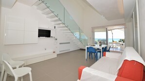 A modern kitchen with a built-in TV, white cabinetry, and a glass staircase leading to a balcony with a view of the sea. - Al004 La Dimora di Venere Villa Frontemare (Alcamo)