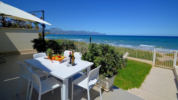 A patio with a table set for dining, a white umbrella, and a view of the ocean. - Al004 La Dimora di Venere Villa Frontemare (Alcamo)
