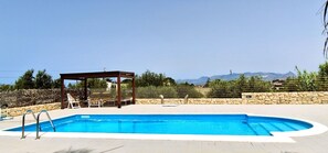 Une piscine agrémentée d’un gazebo en bois, de chaises longues et d’un mur en pierre.