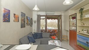 A living room with a grey sofa, a coffee table, and a TV on a wooden cabinet. There are paintings on the wall and a window with a view of a snowy landscape. - Casa Rudi in Sirmione (Sirmione)