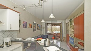 A modern kitchen with white cabinets, a dining area with a grey sofa, and a view of a snowy landscape through the door. - Casa Rudi in Sirmione (Sirmione)