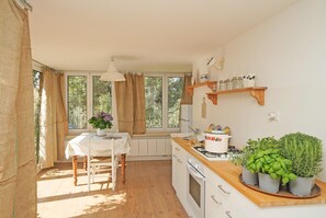 Cozinha com bancada de madeira, armários brancos, mesa de jantar com uma cadeira e janela com cortinas.