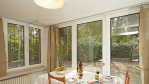 A dining area with a table set for two, featuring a bottle of wine, a bowl of fruit, and a book.