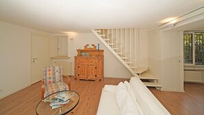 A living room with a sofa, a wooden cabinet, a glass table with magazines, a staircase, and a door.