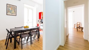Un coin repas avec une table et des chaises, une cuisine à l’arrière-plan et un couloir menant à une autre pièce.