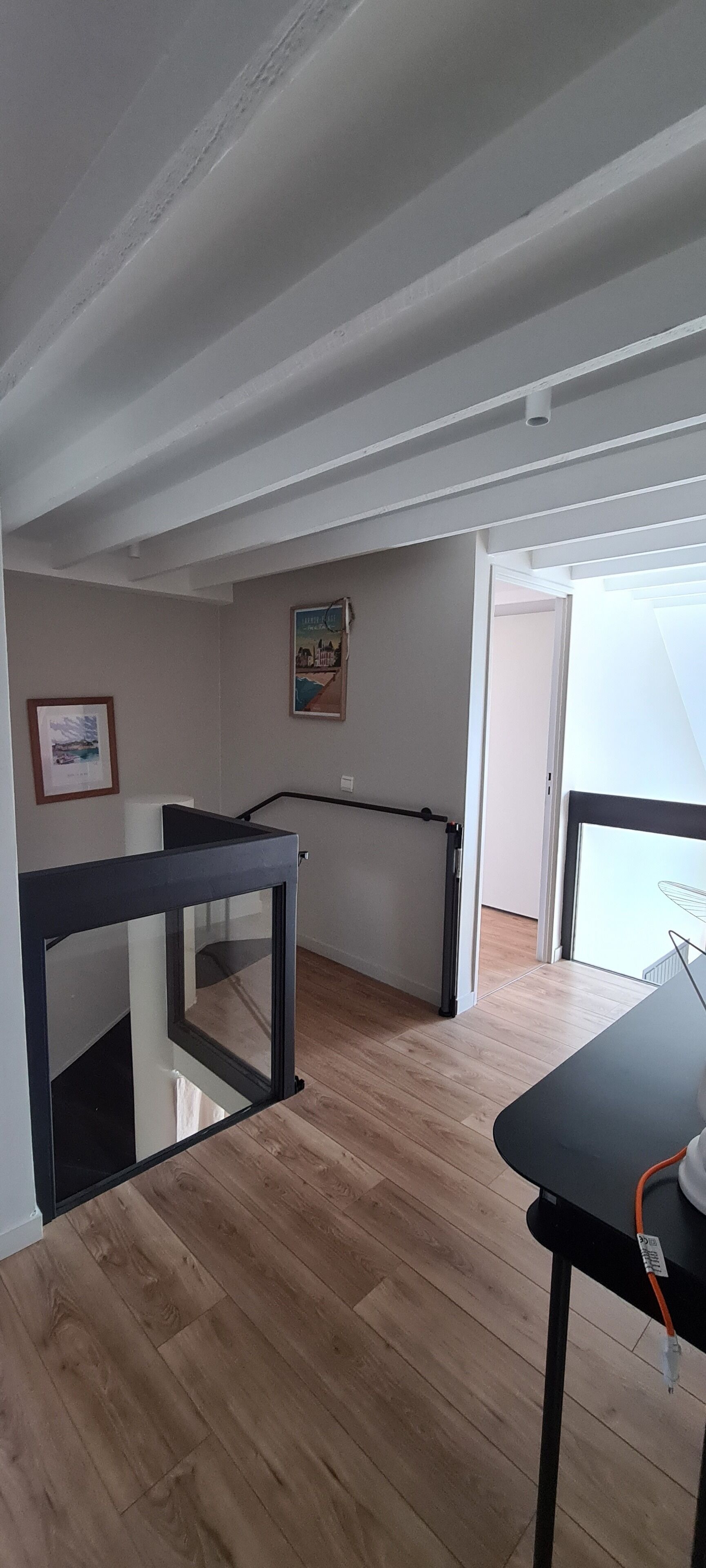 A room with a wooden floor, a black table, and a glass partition. There is a door leading to another room and a window with a view.