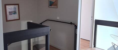 A room with a wooden floor, a black table, and a glass partition. There is a door leading to another room and a window with a view.