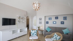 A living room with a flat-screen TV, white shelving, wicker chairs with blue cushions, a grey sofa with teal cushions, and a unique spherical chandelier. - Casa Giovannina - Charming Fisherman s House With Stunning Views (Conca dei Marini)