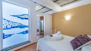 Un dormitorio con cama, toallas, un cojín morado y una pintura de un paisaje nevado.