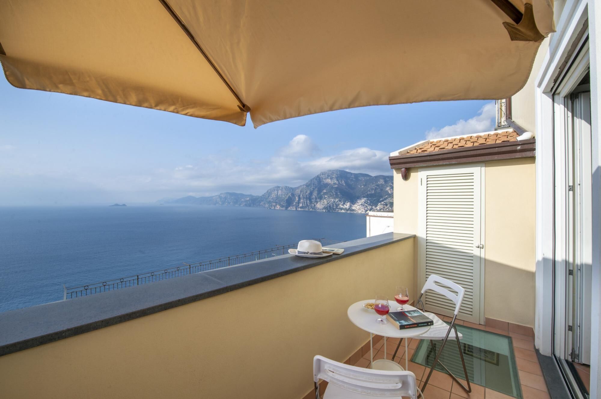 Un balcón con mesa, sillas y vistas al mar y a las montañas.