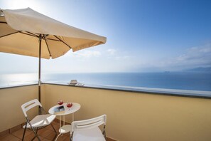 Un balcon avec une table, des chaises et un parasol, offrant une vue sur la mer.