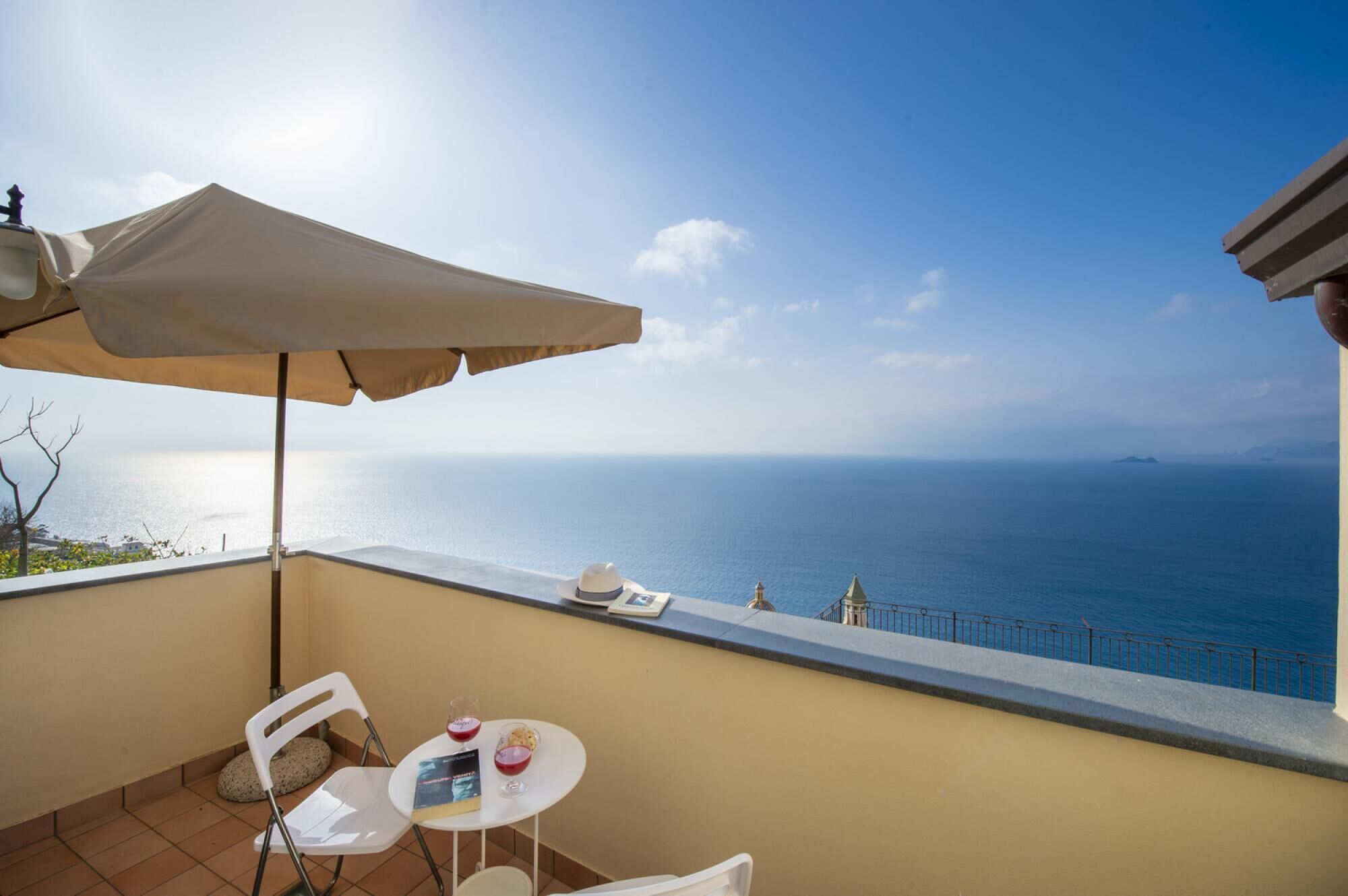 Un balcon avec une table, des chaises et un grand parasol, offrant une vue sur la côte.