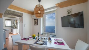 Un comedor con una mesa preparada para cuatro, un ventanal con vistas y un televisor fijado a la pared.