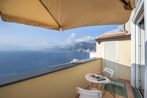 A balcony with a table, chairs, and a table umbrella overlooking the sea.