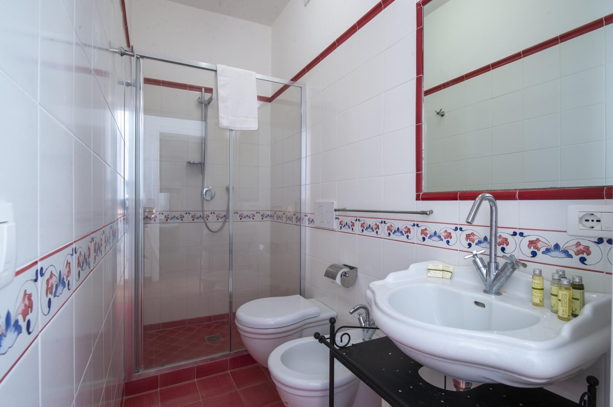 Et badeværelse med glas brusekabine, toilet, bidet og vask med toiletartikler.