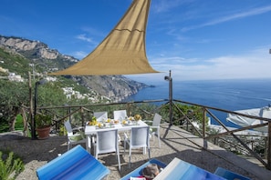 A terrace with a table set for two, overlooking a coastal landscape with a clear view of the sea and a mountainous backdrop. - Casa Punta Paradiso - Hot Tub and Panoramic Garden (Praiano)