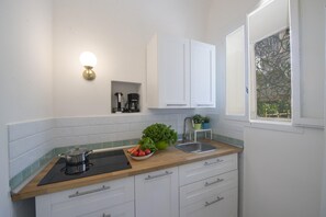 A kitchen with white cabinets, a wooden countertop, a sink, a stove, and a window with a view of greenery.
