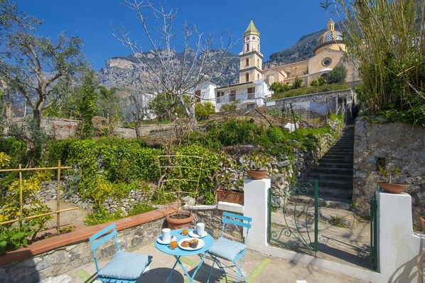 A terrace with a table and chairs, a stone wall, and a view of a church with a bell tower.