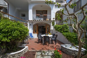 A courtyard with a round table and chairs, surrounded by plants and a stone wall.